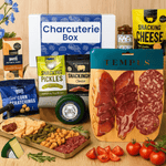 Charcuterie box with various food items including meats, cheeses, and pickles on a wooden surface.