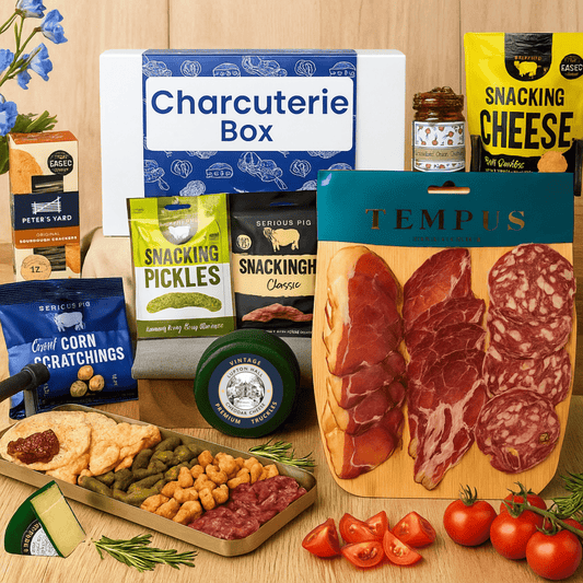 Charcuterie box with various food items including meats, cheeses, and pickles on a wooden surface.