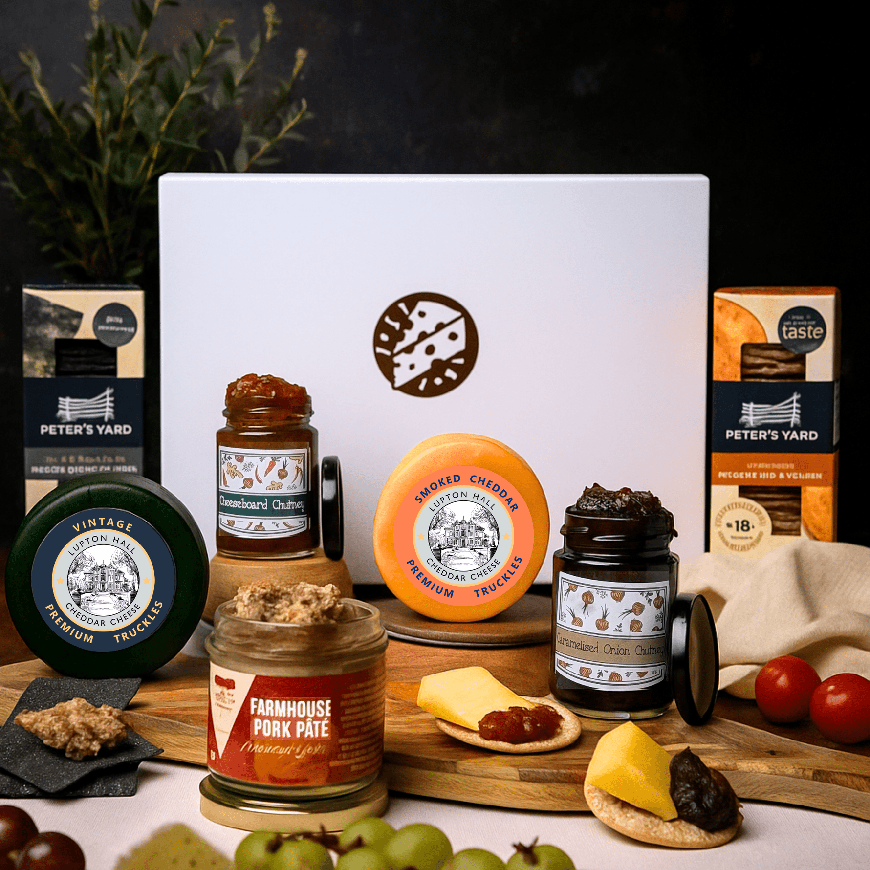 Assorted food products including cheese and pate gift, chutneys, and other spreads on a wooden board with a dark background.